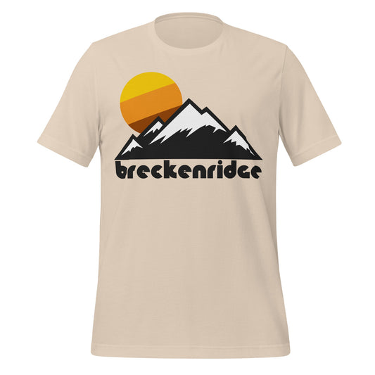 A vintage, souvenir Breckenridge soft cream colored t-shirt with an image of a stylized mountain landscape, complete with multiple snow covered peaks, and a setting warm toned sun in bright yellows and oranges. In reference to Breckenridge, Colorado's popular Breckenridge Ski Resort, known for its world class skiing. 