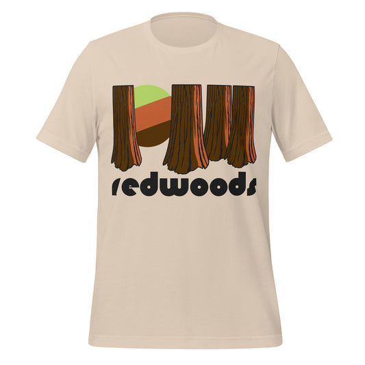 A retro, souvenir soft cream t-shirt with a picture of a forest with large tree trunks and a setting green, red, and brown sun setting. Says "redwoods" in reference to California's Redwood National Park, home to the world famous and endangered redwood trees. 