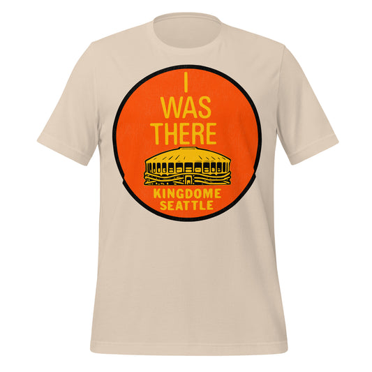 A soft cream 70s style t-shirt that says "I Was There" with an image of a stadium in yellow, the "Kingdome Seattle", where the Seattle Seahawks NFL team, Seattle SuperSonics NBA team and the Seattle Mariners MLB team played until it was demolished in 2000. Officially known as King County Stadium. 
