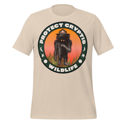 A soft cream vintage short sleeved t-shirt that says "Protect Cryptid Wildlife". Has sun, moon, and star symbols. Image of mythical creature in a forest with a hat that says cryptid and a pink and orange sunrise. 