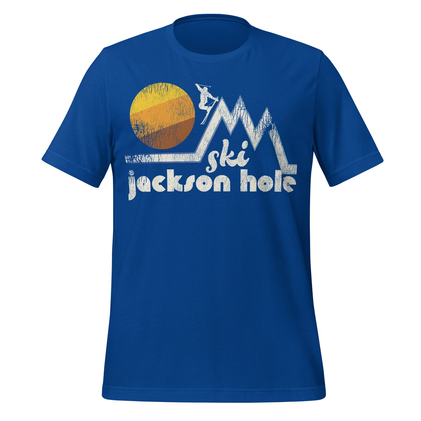 A true royal blue colored retro t-shirt that says "Ski Jackson Hole", referencing the Wyoming city, underneath the image of multiple white triangular mountain peaks with a skier, a circular striped yellow, orange, and brown sun behind the ski and snowboarding slopes. 