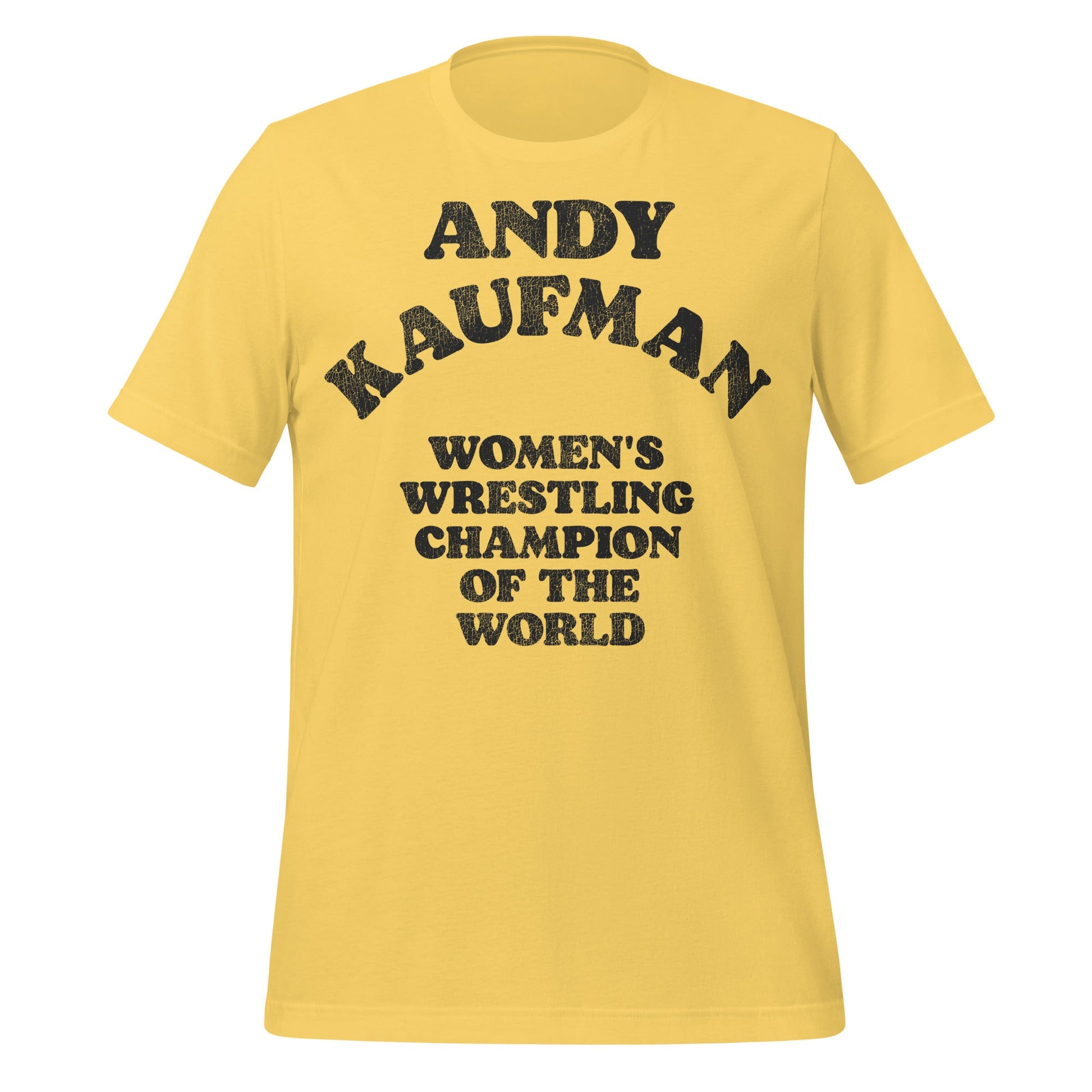 A yellow retro 80s style t-shirt that says "Andy Kaufman", "Women's Wrestling Champion of the World". From the 2025 biopic movie Queen of the Ring about Mildred Burke directed by Ash Avildsen. 