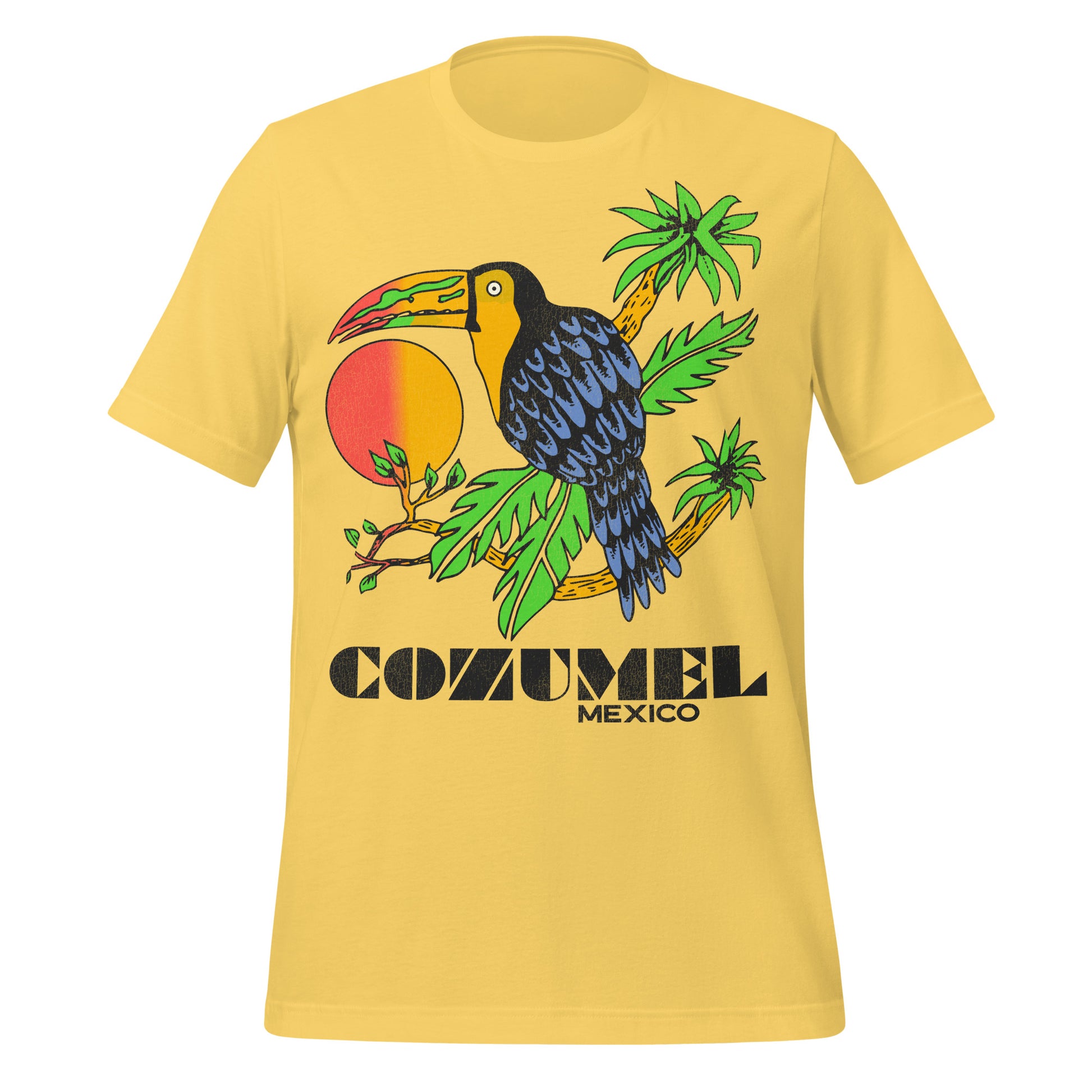 A yellow retro t-shirt that has a toucan bird with blue black feathers and a green, red, and yellow beak sitting on bright green palm tree leaves, a sunset in the background. Shirt says Cozumel Mexico, the tourist resort island in the Carribean. 